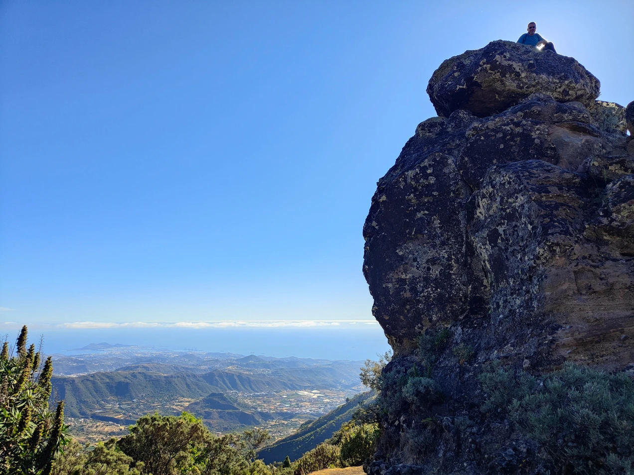 hombre encima de una roca con un paisaje panorámico desde la montaña hasta el mar